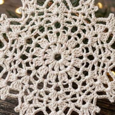 Ultra close up macro photography of handmade delicate ivory cotton crochet snowflake Christmas ornament on rustic wood with fairy lights