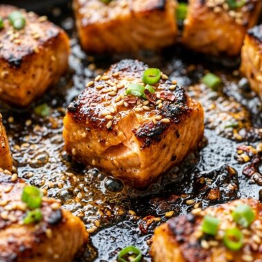 Crispy honey garlic butter salmon bites sizzling in cast iron skillet with sticky golden glaze
